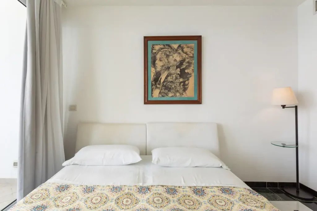 Bedroom with white bed, artwork and air conditioning