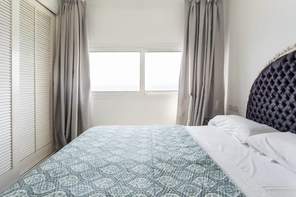 Bedroom with dark curved headboard and a sea-facing window