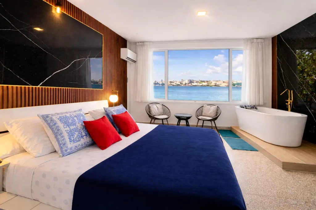 Water-view bedroom with a blue bed and freestanding tub at Penthouse Rio Mar